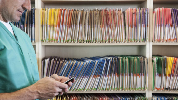 A dentist checking his cell phone with file folders in the background.