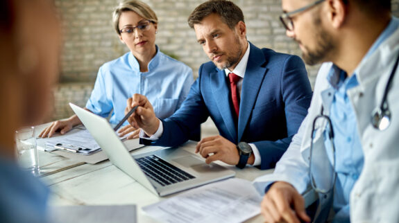 Mid adult businessman and group of doctors working on a computer during a meeting.