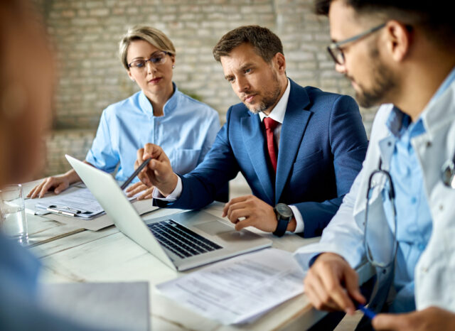 Mid adult businessman and group of doctors working on a computer during a meeting.